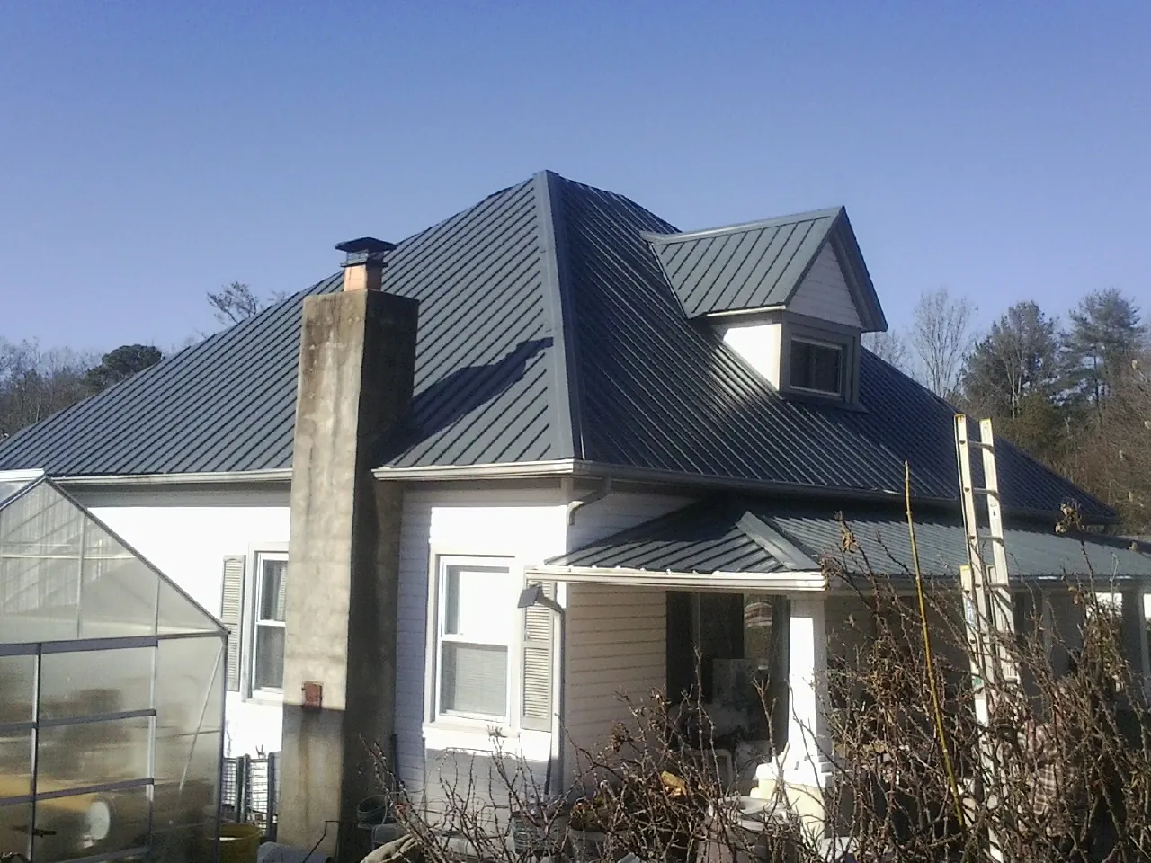 Dark blue standing seam metal roof on a white farmhouse with dormer — Slate & Tile Roof Repair by Roofing Brothers in Saint Michael