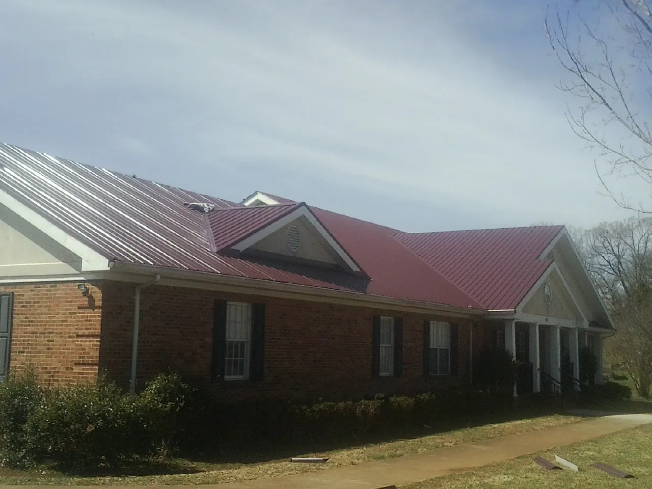 Red metal roof with gabled entries on a long brick building, from a Hail Damage Roof Repair job in Saint Michael
