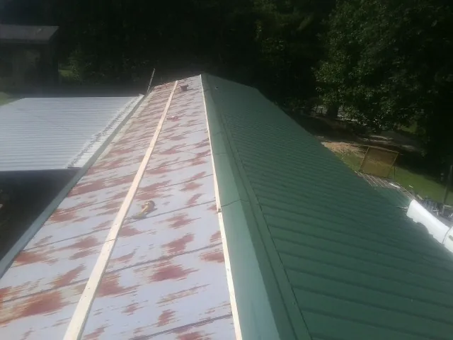 Old rusted panels beside newly installed green metal roofing — Wind Damage Roof Repair by Roofing Brothers in Saint Michael