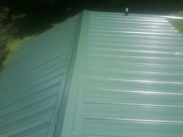New green metal panels meeting at the ridge of a roof — Flat Roof Repair work by our crew in Saint Michael