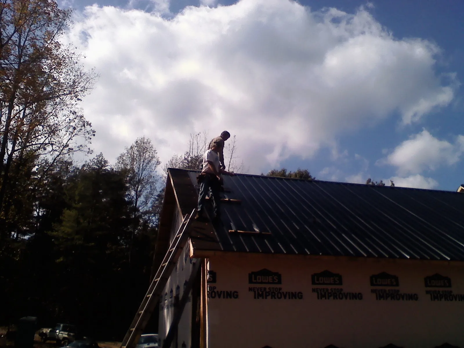 Roofer fastening dark metal panels high against a cloudy sky, from a Roof Inspection job in Saint Michael