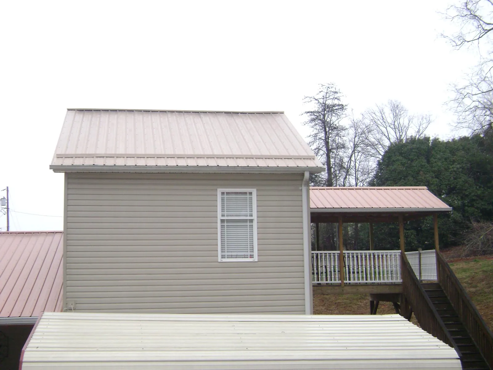 Tan metal roofs on a two story addition and attached porch, from a Roof Replacement job in Saint Michael